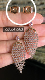 تصویر جفت گوشواره ژوپینگ اورجینال روی دست، با طراحی بال فرشته، نگینهای اتمی سفید و شفاف با کاشت معکوس، آبکاری طلایی و نمای نزدیک پشتهای سوزنی برای نمایش جزئیات و اثبات اصالت ژوپینگ
