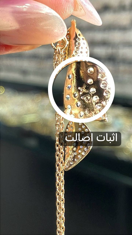 نمای نزدیک نشان XP حکشده در پشت برگ و آثار مخراجکاری در پشت گوشواره ژوپینگ با زنجیرهای فلزی طلایی